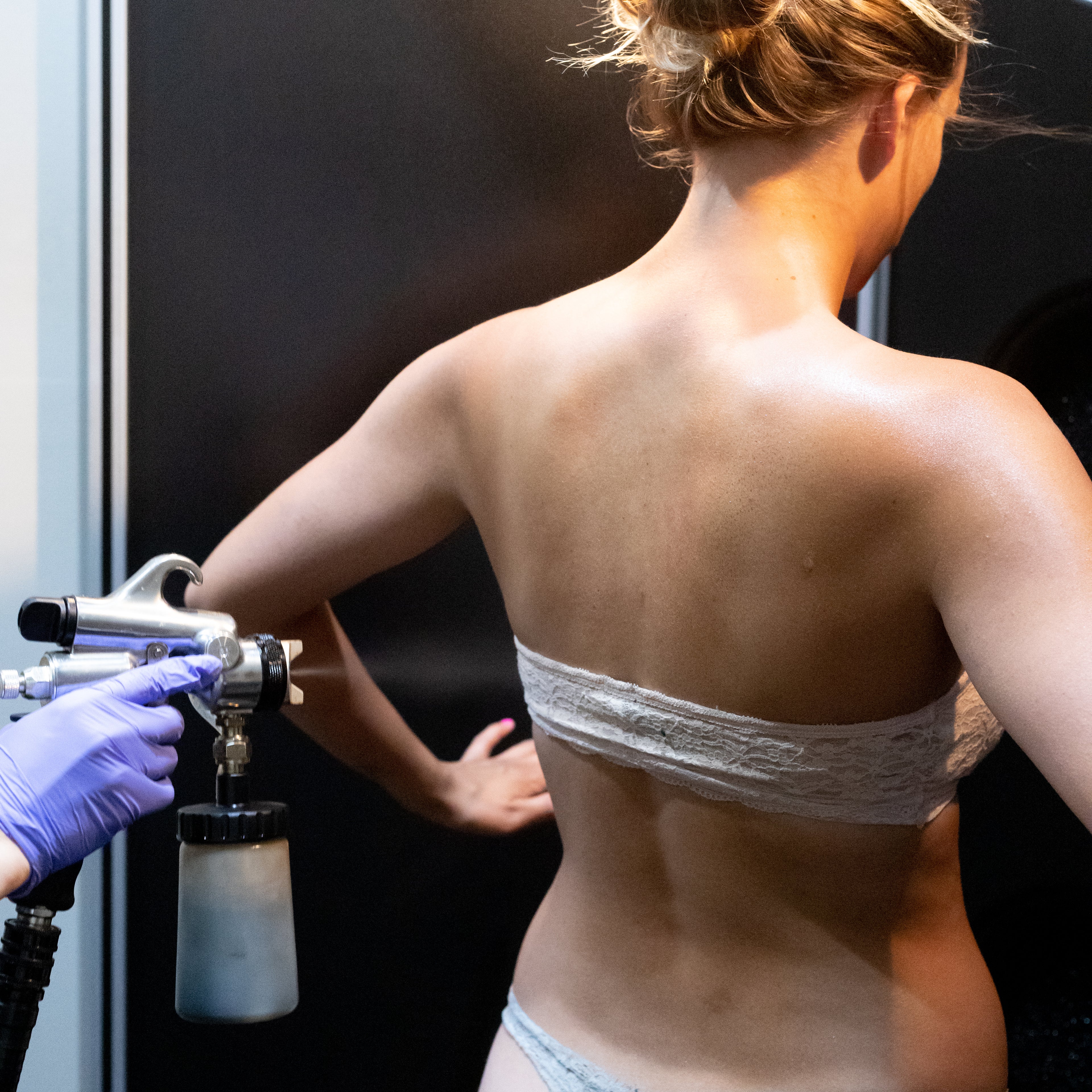 Person receiving a spray tan on their back with a professional spray tan gun.